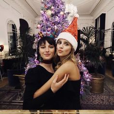 two women hugging each other in front of a christmas tree with lights and decorations on it