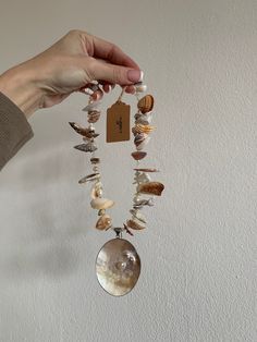 a person holding a necklace with shells and seashells on it, in front of a white wall