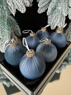 four blue christmas ornaments sitting on top of a black tray next to evergreen branches and pine cones