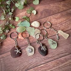 five different sea glass keychains on a wooden table next to plants and seashells