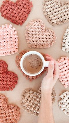 a person holding a cup of coffee in front of crocheted hearts