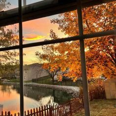 the view from an open window looking out onto a lake and trees with orange leaves