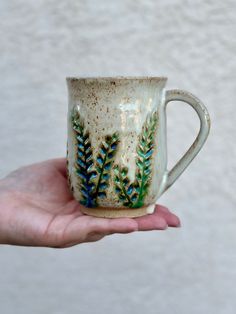 a hand holding a coffee cup with blue and green designs on it's side