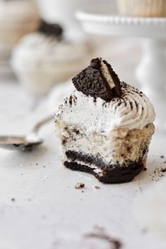 a cupcake with oreo cookies and cream frosting is on the table next to a spoon