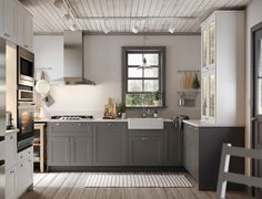 a kitchen with gray cabinets and white walls, wood floors and a window in the center