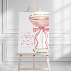 a welcome sign with a pink bow on it in front of a white wall and wooden easel