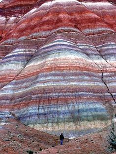 a man standing in front of a colorful rock formation on the side of a mountain