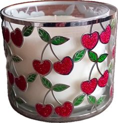 a glass candle holder decorated with red and green hearts, leaves and berries on a white background