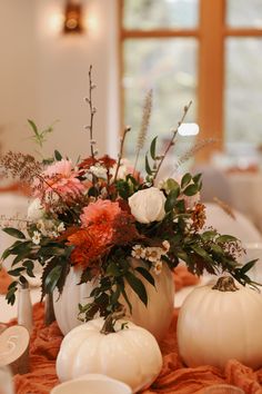 a table topped with white pumpkins and flowers on top of a cloth covered table