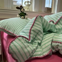 a stuffed animal sitting on top of a bed with green and white striped sheets in front of a window