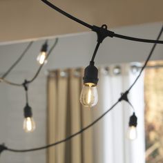 some light bulbs are hanging from a black wire in front of a window with curtains