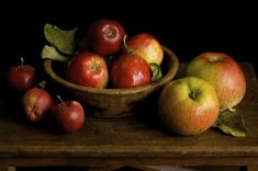 a painting of apples in a bowl on a wooden table next to leaves and a knife