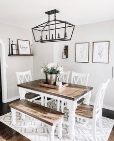 a dining room table with white chairs and wooden benches in front of the light fixture