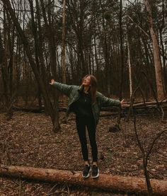 a woman is standing on a log in the woods with her arms spread wide open