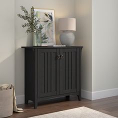 a small cabinet with a vase on top next to a lamp and rug in a room