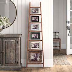 an old wooden ladder stands in front of a white painted wall with pictures on it