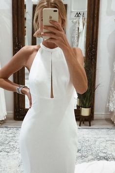 a woman taking a selfie in front of a mirror wearing a white halter dress