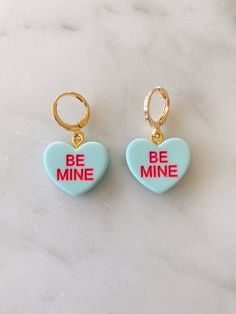 Obsessed is an understatement! Pay homage to your favorite Valentine's Day candies with these adorable be mine huggies. Available in both pierced hoops or clip on styles (for those without their ears pierced) these earrings are super fun and eye catching. Choose from a matte candy heart in a number of different colors or a two color glitter heart. The perfect size they are noticeable without being overwhelming. The charms are lightweight and easy to wear. Hoops are gold plated and nickel free. M Cute Dangle Hoop Earrings For Valentine's Day, Cute Huggie Hoop Earrings For Valentine's Day, Cute Huggie Jewelry For Valentine's Day, Valentine's Day Cute Huggie Hoop Earrings, Trendy Huggie Heart Earrings For Valentine's Day, Valentine's Day Cute Dangle Hoop Earrings, Cute Heart Charm Huggie Earrings, Cute Huggie Earrings With Heart Charm, Cute Heart Hoop Earrings For Gift