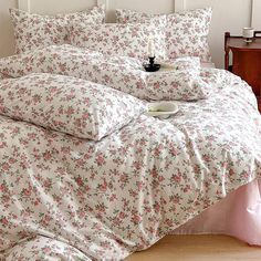 a white bed with pink flowers on it and a tea cup sitting on the pillow