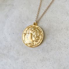 "Please view the photos! This pendant is much larger than our other pieces! A gorgeous gold highly detailed Persephone coin with a charioteer on the back. The beautiful piece offers options! Beautiful on its own or layer with our other pieces.  Size: 30\" Chain 35mm pendant  Note: This is a very large pendant. We recommend the longest length of chain for this piece to look proportionate. Please view the photos prior to ordering. Specs: 24k gold plated brass Simple wearable design  Easy to use clasp Wear and Care: Do not wear in the water. Do not use harsh cleansers on your jewelry. Simply wipe clean with a polishing cloth. Keep jewelry dry." Gold-tone Gold-plated Coin Pendant Necklace, Gold-tone Coin Shaped Necklace, Gold-tone Coin Shaped Jewelry Pendant, Mythological Style Gold Coin Pendant Jewelry, Gold-tone Brass Coin Pendant Necklace, Wearables Design, Summer Necklace, Coin Necklace, Keep Jewelry