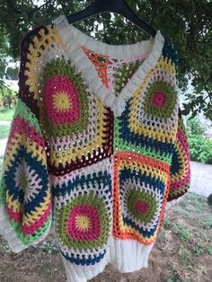 a colorful crocheted sweater hanging on a clothes hanger in front of a tree