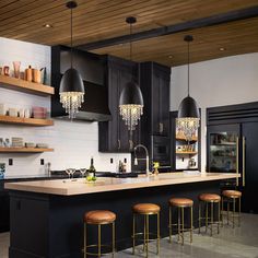 a kitchen with black cabinets and gold bar stools in front of an island counter