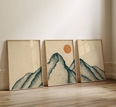 three framed art pieces on the floor in front of a wall with a mountain scene