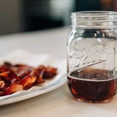 a glass jar filled with liquid sitting on top of a table next to a plate of food