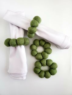 two white napkins with green felt balls on them and one rolled up in the shape of a wreath