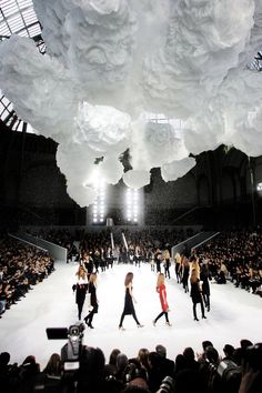 models walk down the catwalk in front of an enormous chandelier hanging from the ceiling