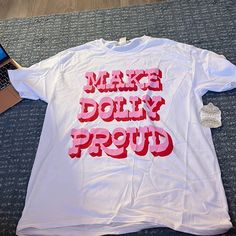 a white t - shirt that says make dolly proud on the front with pink letters