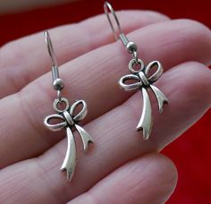 "Antique silver tone small bow knot charm earrings. Small bow charms dangling from stainless steel earring hooks. Earring length: 38mm; 1.5\" (including the earring hook) Earring hook material: stainless steel Charm material: Zinc alloy, Nickel safe, Lead free This listing is for one pair of bow earrings with rubber backs. This earring will come in a gift bag. I offer combined shipping costs which give you a shipping discount for ordering multiple items from my shop. Earrings care: Take them off Dangle Bow Earrings For Gift, Metal Bow Earrings For Gifts, Dangle Bow Jewelry As Gift, Dangle Bow Jewelry For Gifts, Silver French Hook Earrings As Gift, Silver Metal Earrings With Bow, Silver Earrings With French Hook For Gift, Silver Bow Dangle Jewelry, Silver Dangle Jewelry With Bow Detail