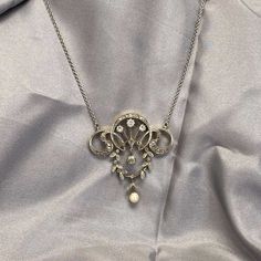 This stunning antique pendant from the Edwardian era features a delicate floral design, embellished with a combination of rose cut and old European cut diamonds, Dangling from the pendant is a natural pearl. This necklace, dating back to the Edwardian era around 1910, is made of platinum on gold. The pendant has an approximate dimension of 1.75 inches x 1.50 inches.  ✦  NECKLACE SPECIFICATIONS: Center Stone: Diamond Diamond Cut: Old European and Rose Cut Age: Antique Edwardian Era, Circa 1910 Pe Victorian White Gold Pendant Necklace, Antique White Gold Pendant Necklace, Antique Round Necklace With Diamond Accents, Victorian White Gold Medallion Necklace, Antique Round White Gold Necklace, Antique White Gold Round Necklace, Antique White Gold Necklace With Diamond Accents, Antique White Gold Necklace With Intricate Design, Victorian Evening Necklace With Hallmark