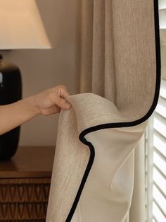 a person is pulling up the curtains in front of a table with a lamp on it