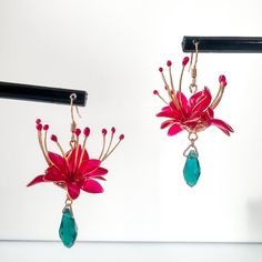 two pairs of earrings with flowers and stones hanging from hooks on a white wall background