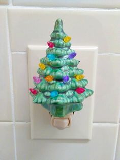 a green christmas tree light switch cover on a white tile wall with colorful lights around it