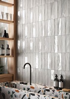 a bathroom with white tiles and wooden shelves on the wall, along with soap dispensers