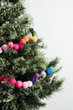 a christmas tree decorated with pom - poms and colored balls is shown in front of a white wall