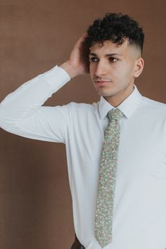 a young man wearing a white shirt and green floral tie with his hand on his head