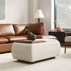 a living room filled with furniture and a white ottoman next to a large painting on the wall