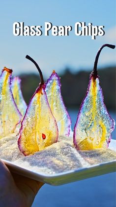 three glass pears sitting on top of a white plate next to water and trees