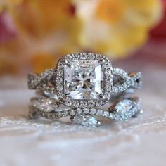 two wedding rings with an engagement ring set on top of each other, surrounded by flowers