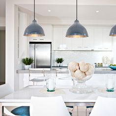 a white kitchen with blue accents and pendant lights hanging over the countertop, surrounded by chairs