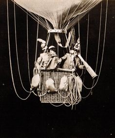 two people in a hot air balloon being lifted from the ground by parachutes and wires