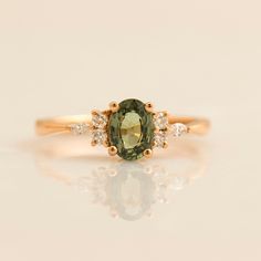 an oval green and white diamond ring with three diamonds around the band, set in yellow gold