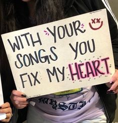 a woman holding a sign that says with your songs you fix my heart