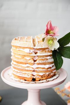 a white cake topped with frosting and flowers on top of a pink pedestal next to other desserts