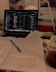 a laptop computer sitting on top of a desk next to a notebook and cup of coffee