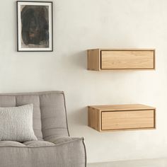 two wooden shelves are on the wall above a gray couch in a white living room