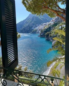 an open window looking out at the ocean and mountains with trees in front of it